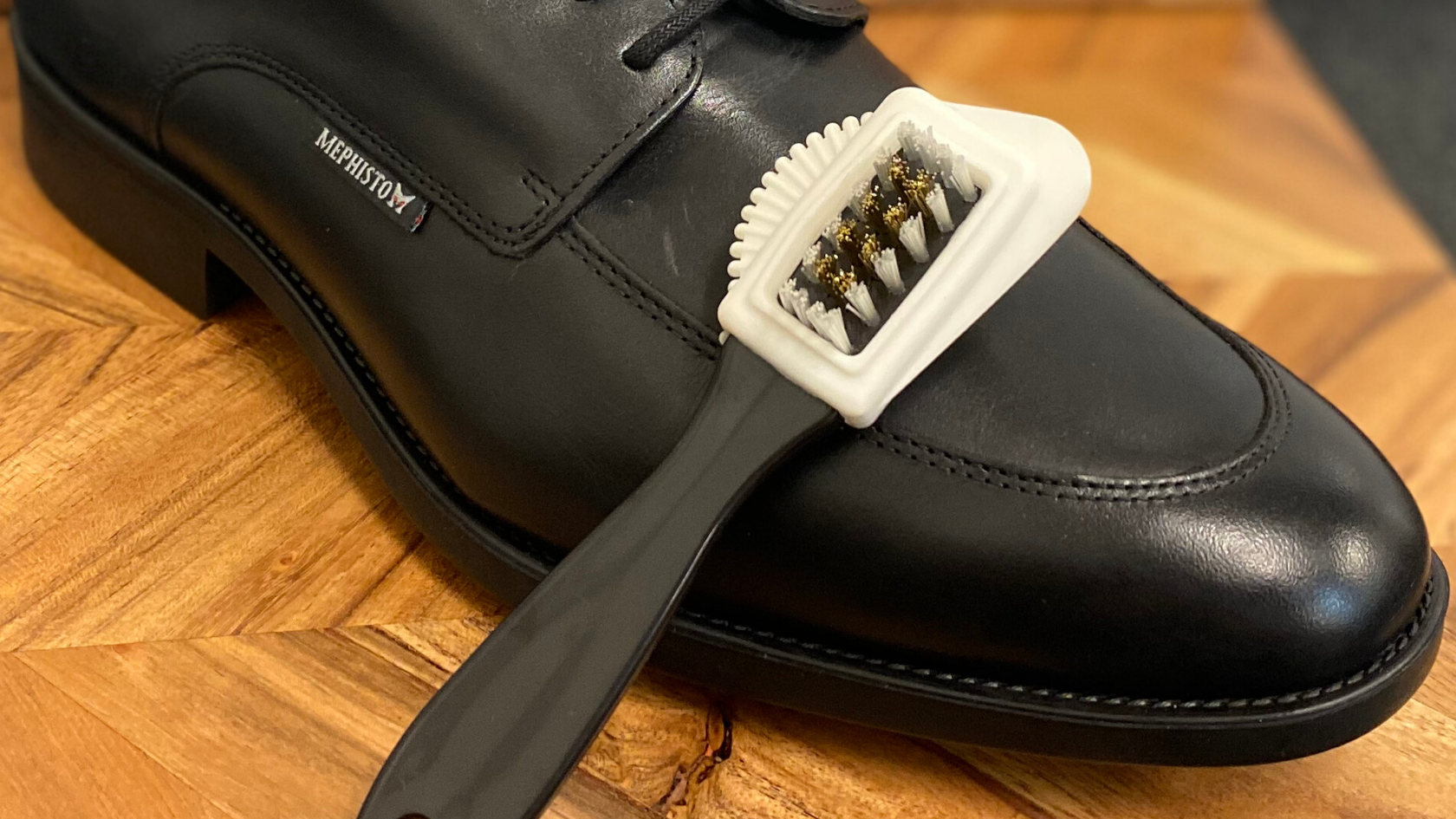 Black leather lace-up with a cleaning brush alongside it.