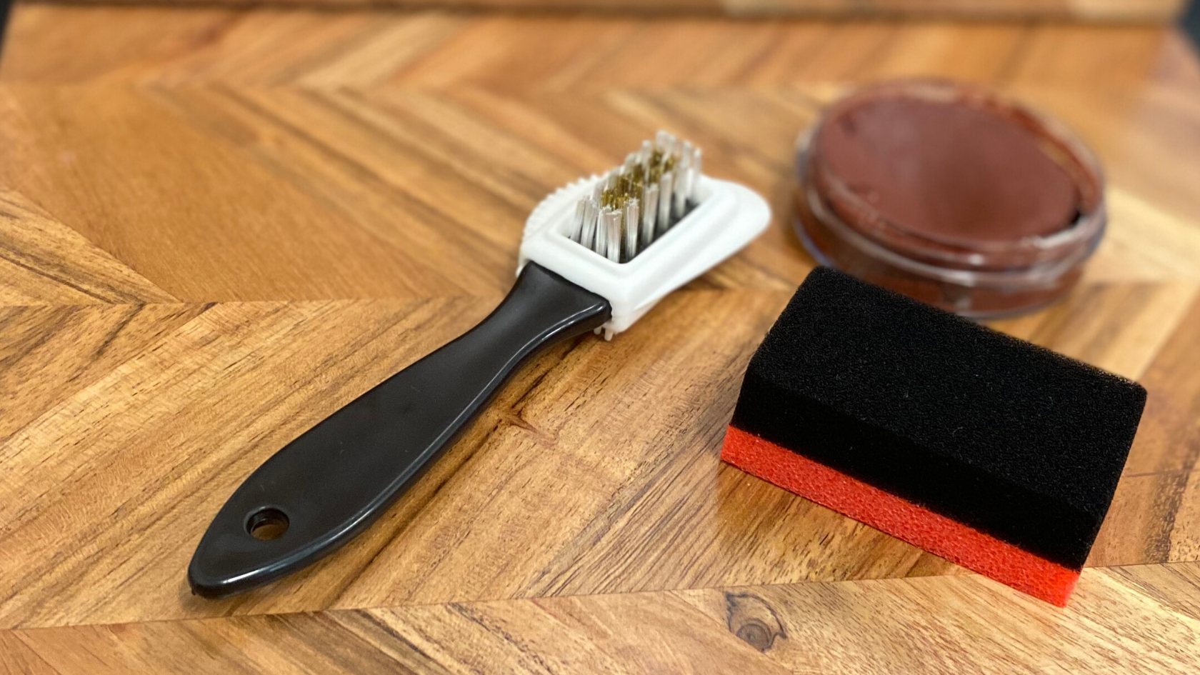 Shoe polish, a shoe cleaning brush and a buffing sponge against a wooden background.